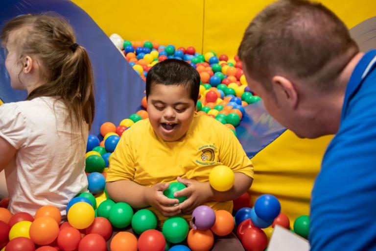 Two young people, supported by an adult playing in a ball pool