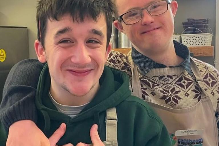 Two young men wearing aprons and smiling at the camera.