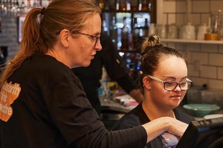 A women showing a young girl how to use a till in a café 