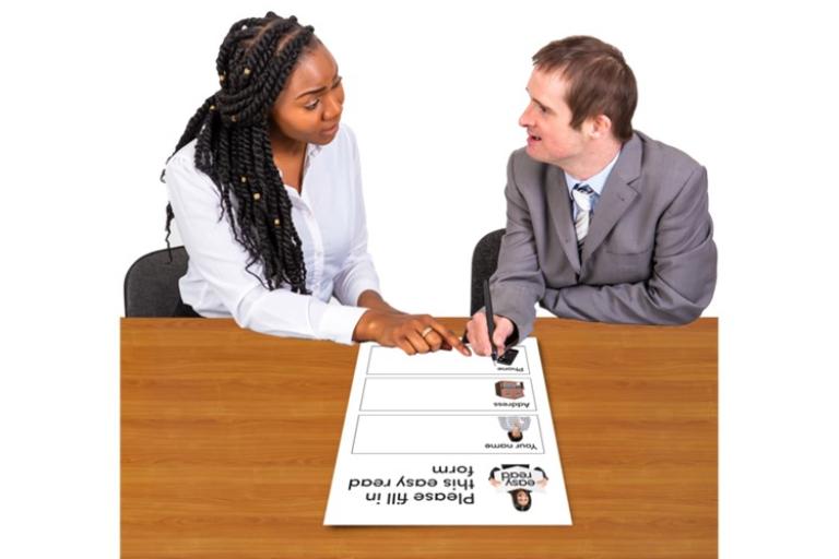 Two people wearing work clothes filling out a form together.