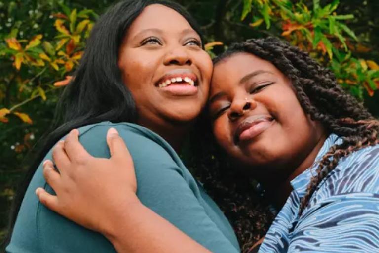 A woman and young person smiling and hugging outside