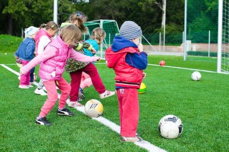 A row of young children kicking footballs on a football pitch