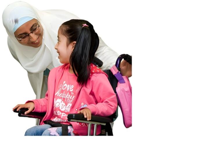 Woman in headscarf smiling at a girl in a wheelchair wearing a pink jacket.