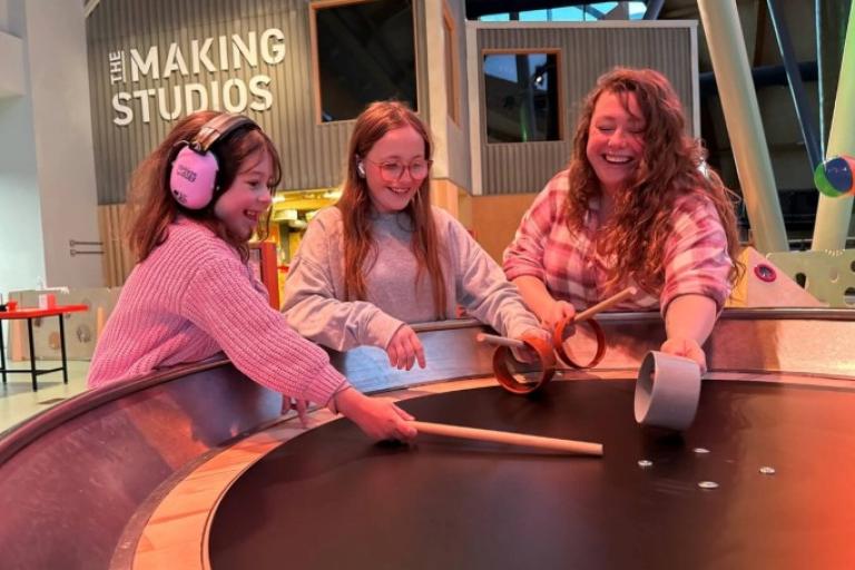 Two smiling girls, one of them with ear defenders, and a women at Life Science Centre