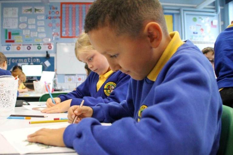 Two primary school students in a classroom holding pencils completing school work. 