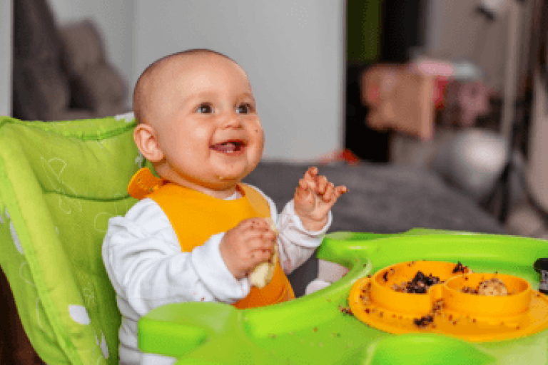 Happy baby in highchair eating food