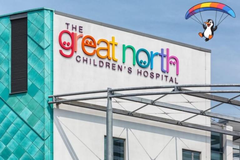 The outside of the Great North Children's Hospital with a cartoon penguin holding a parachute in the sky.