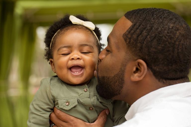 Man kissing a baby.  Baby is smiling.