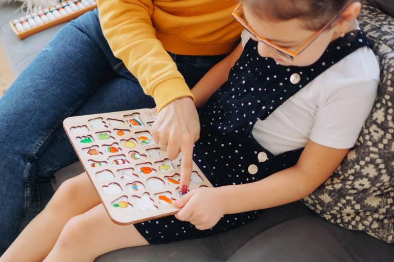 Child sitting with alphabet jigsaw. Adult pointing to letters