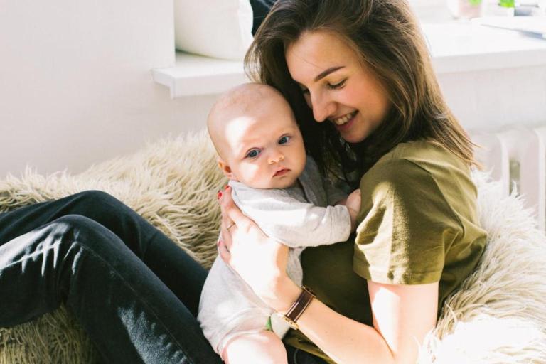 A smiling teenage girl in a green top holding a baby.