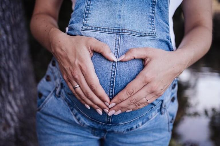 Pregnant woman with hands on tummy, hand making a heart shape